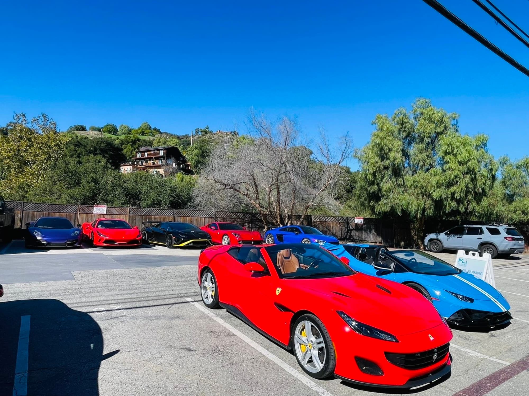 Two convertibles beside an MLI valet parking sign, with a row of supercars behind